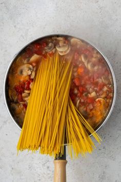 spaghetti being cooked in a pot with mushrooms and tomato sauce on the side, next to a wooden spatula