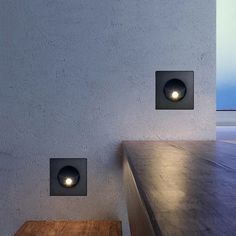 two square lights on the side of a wall next to a wooden table and bench