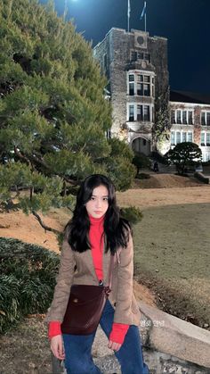 a woman is posing for a photo in front of a building with trees and bushes