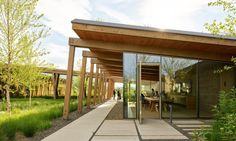 an outdoor dining area with glass walls and wooden posts on the outside, surrounded by green grass