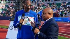 two men standing next to each other in front of an olympic flag on a track