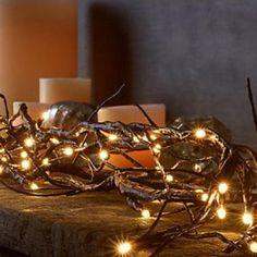 some candles are sitting on a table with branches and lights all around the place in front of them