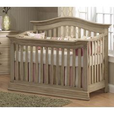 a baby crib with pink and white bedding in a room next to a dresser