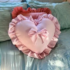 a heart shaped pillow on top of a bed with ruffles in the shape of a bow