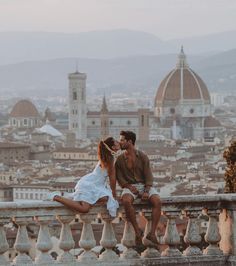 a man and woman sitting on top of a building next to each other