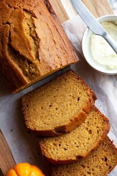 sliced loaf of pumpkin bread on a cutting board next to oranges and whipped cream