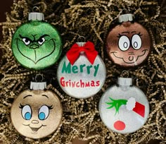 four christmas ornaments with cartoon faces on them sitting in some hay and straw, all decorated to look like they are smiling