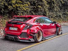 a red sports car parked on the side of the road next to some green trees