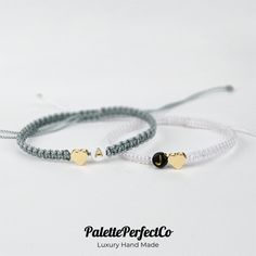 two bracelets with gold heart charms on white string and black beaded cord are shown