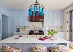 a large kitchen with blue cabinets and white counter tops, two stools are in front of the island