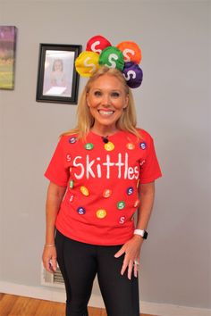 a woman wearing a red shirt with the words skittles on it and balloons above her head