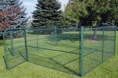 a large green dog kennel in the middle of some grass with trees behind it