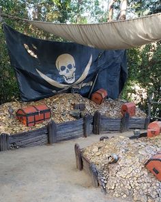 a pirate themed area with logs, rocks and an old flag hanging over it's head