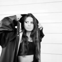 black and white photograph of a woman holding her jacket over her head while standing in front of a wall