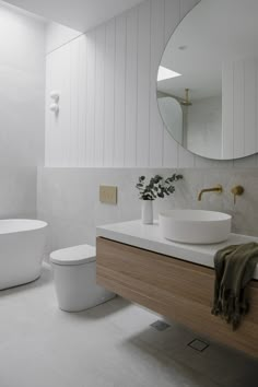 a bathroom with a sink, toilet and bathtub next to a round mirror on the wall