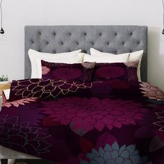 a bed with purple and white flowers on it, next to a night stand lamp