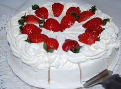 a white cake topped with strawberries on top of a lace doily next to a knife