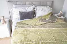 a bed with green and white bedspread on top of it next to a night stand