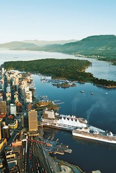 an aerial view of a city with ships in the water and mountains in the background