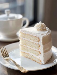 a slice of white cake on a plate with a fork and cup in the background