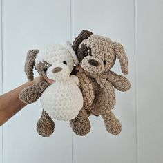 two stuffed animals being held by someone's hand in front of a white wall