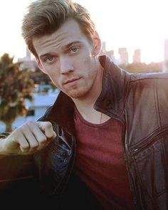 a young man in a leather jacket posing for a photo with the city behind him