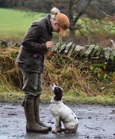 a man standing next to a white and black dog on a wet ground near a fence