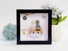 a couple is sitting on a bench with flowers in the vase behind them and an anniversary card attached to it