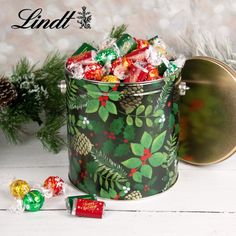 a christmas tin filled with assorted candies next to pine cones and candy canes