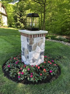 a lamp on top of a stone pillar in the middle of a flower bed with flowers around it