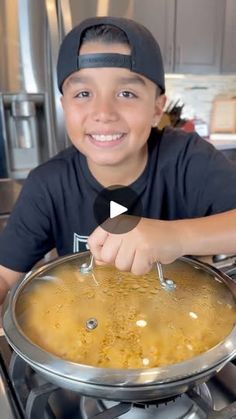 a young boy is smiling while cooking food in a pan on top of the stove