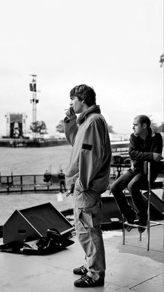 black and white photograph of man standing on pier with other people sitting in the background