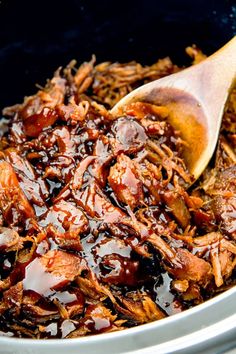 shredded pulled pork in a slow cooker with bbq sauce and wooden spoons