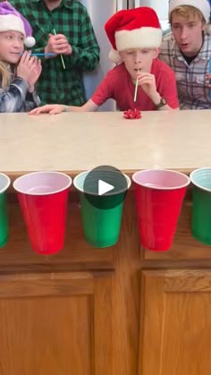 a group of kids sitting at a table with cups in front of them and one boy wearing a santa hat