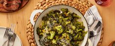 broccoli is in a bowl on a table with silverware and wine glasses