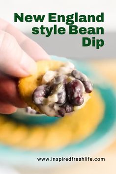 a hand holding a cracker with blueberries and cream on it that says new england style bean dip