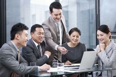 a group of business people sitting around a table with a laptop in front of them