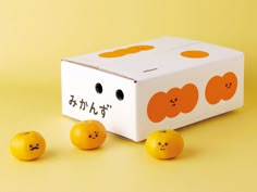 three oranges sitting in front of a box with faces drawn on it