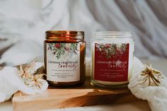 two candles sitting on top of a wooden table next to white flowers and blankets in the background