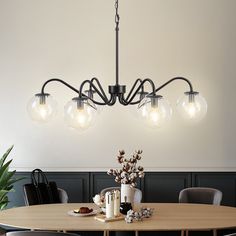 a chandelier hanging over a dining room table with four chairs and a potted plant