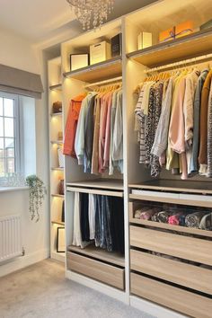 an organized closet with clothes hanging on shelves and chandelier in the corner, next to a window