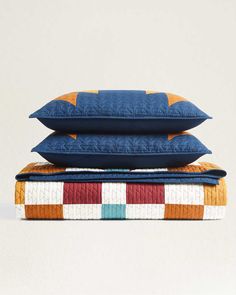 three pillows stacked on top of each other in different colors and patterns, one is orange, the other blue