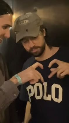 two men standing next to each other with one pointing at the shirt on his chest