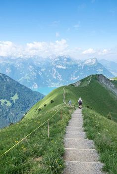 two people are hiking up the side of a steep hill with mountains in the background