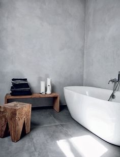 a white bath tub sitting next to a wooden table in a room with concrete walls