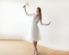 a woman in a white dress holding a flower and pointing to the side with her right hand