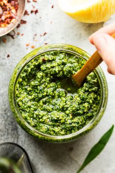 a person dipping pesto into a glass jar with a wooden spoon on the side