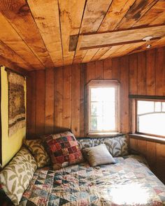 a bed sitting in the corner of a room with wooden walls and ceiling tiles on it