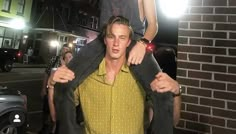 a man holding onto another mans shirt while standing in front of a brick building at night