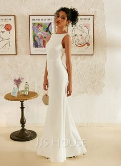 a woman in a white dress standing next to a wall with pictures on it and a table